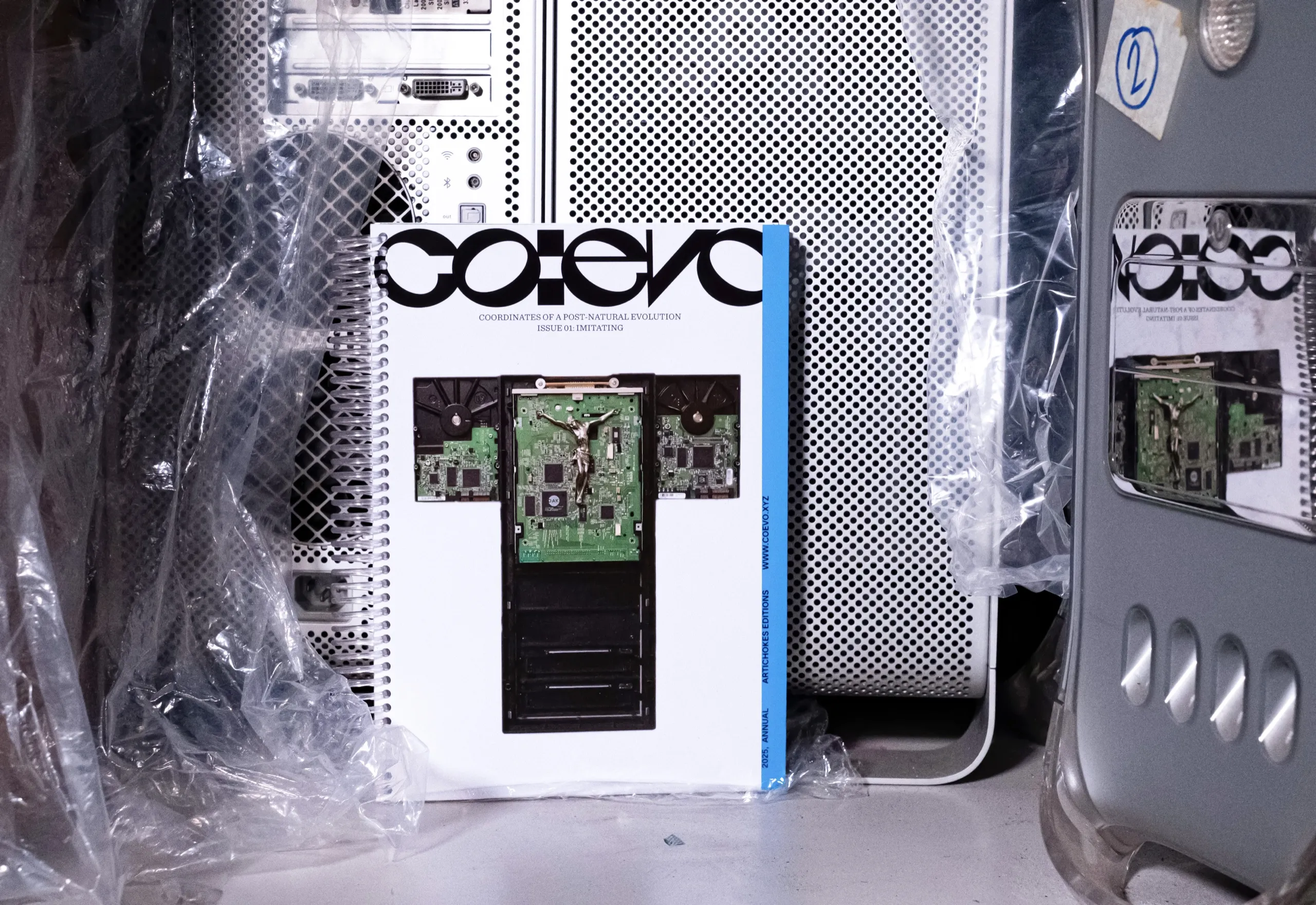 The cover of co:evo, with a crucifix made of circuit boards, leaning against computer cases wrapped in plastic