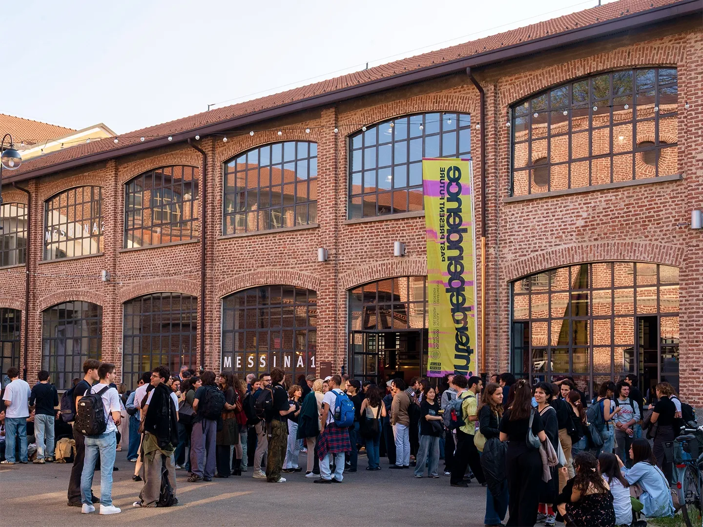 Visitors queuing outside the brick building of the exhibition, with an INTERDEPENDENCE banner