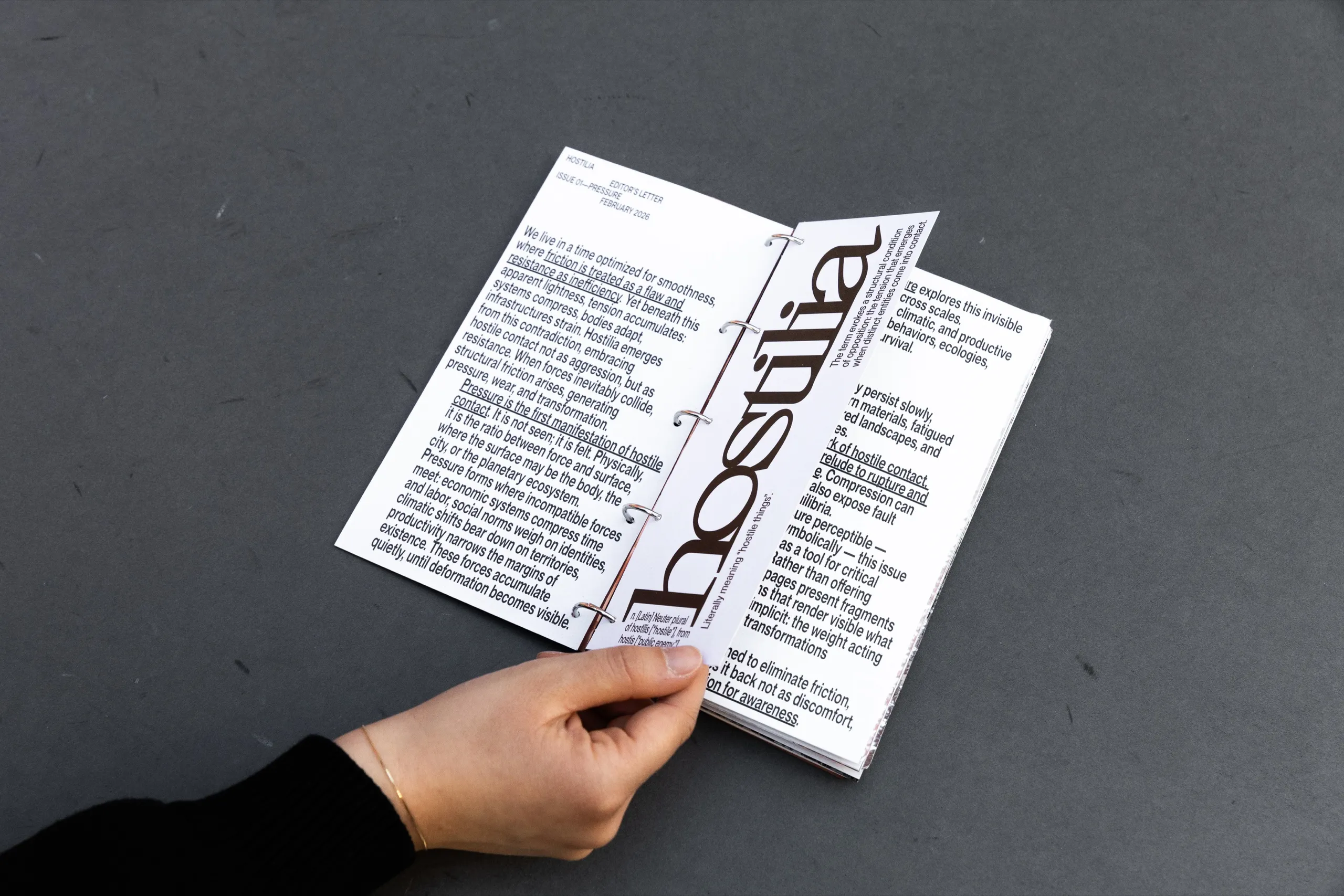 Hands opening Hostilia on the page with the masthead